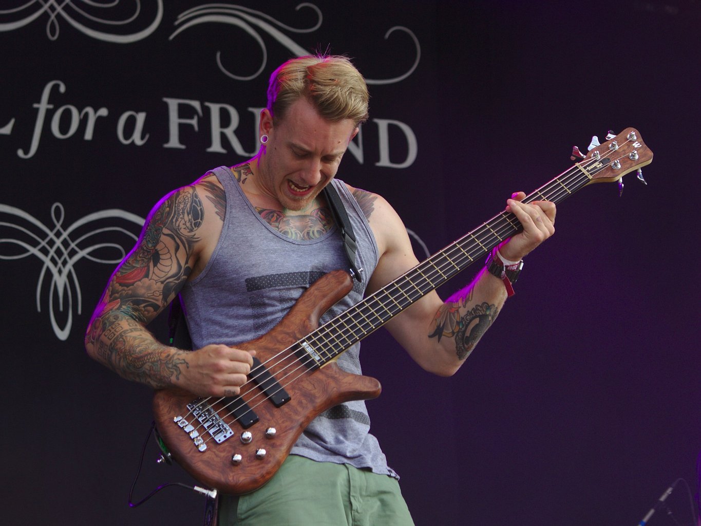 Tattoed bassist in sleeveless top looks at his bass