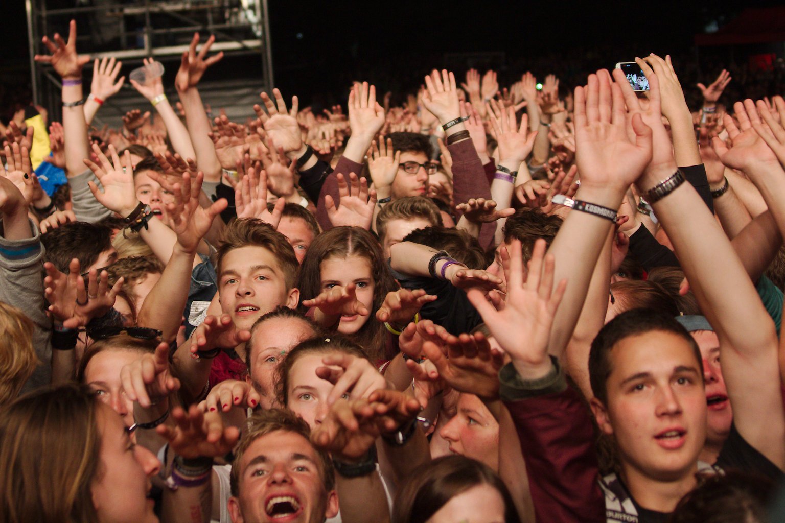 Crowd with raised hands reaching and facing towards the photographer