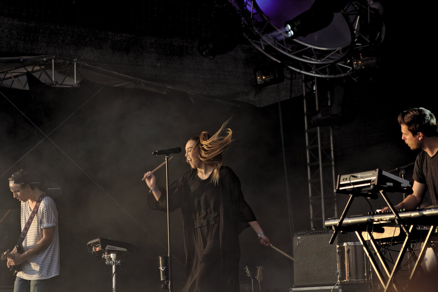 Claire singer Josie is about to hit a drumpad, her hair flying through the air. Guitarist and keyboarder are visible at the edges