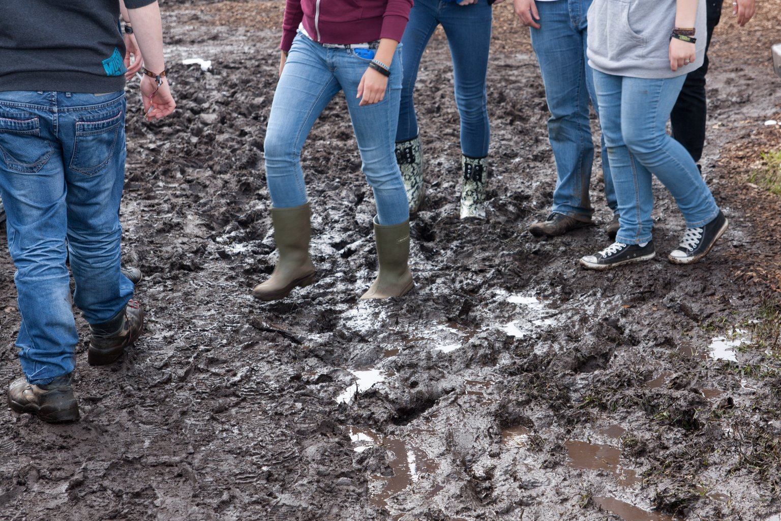 Legs of people at a festival in rubber boots walking through mud